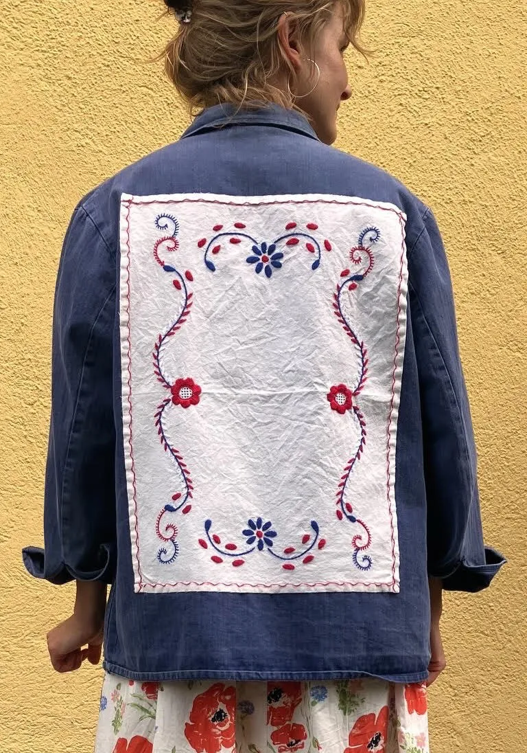 Blue jacket worn from behind, with an embroidered white panel set into the back