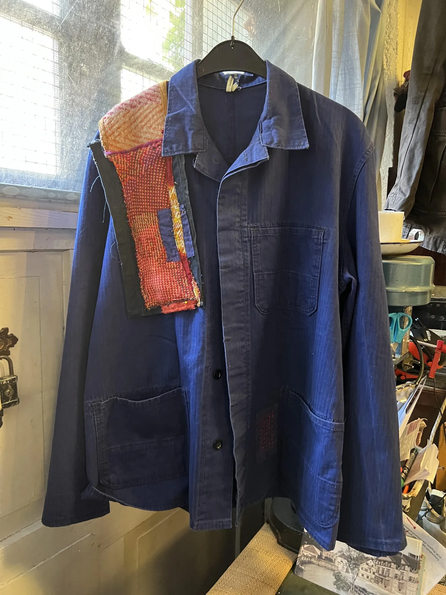 Blue workwear jacket with a panel of orange mesh and patchwork across one shoulder
