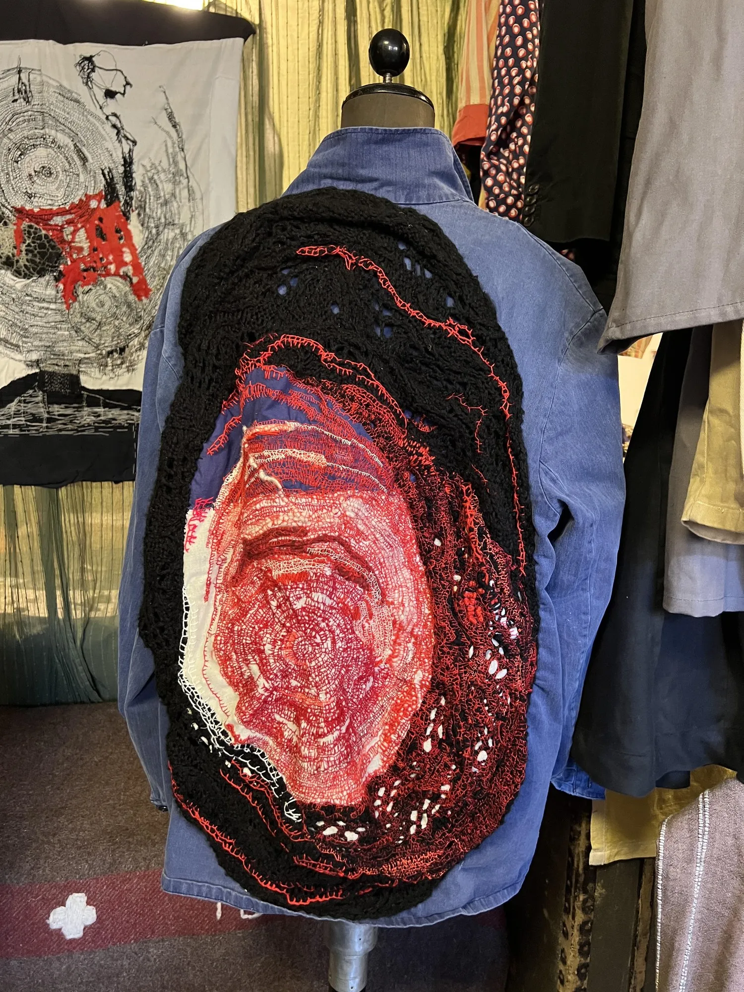 Blue jacket on a mannequin, the whole back worked into a large red and black textile relief