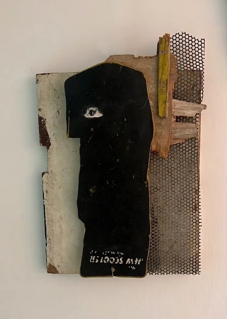 Mixed-media wall piece: a dark figure with a single eye, built on salvaged wood and metal mesh